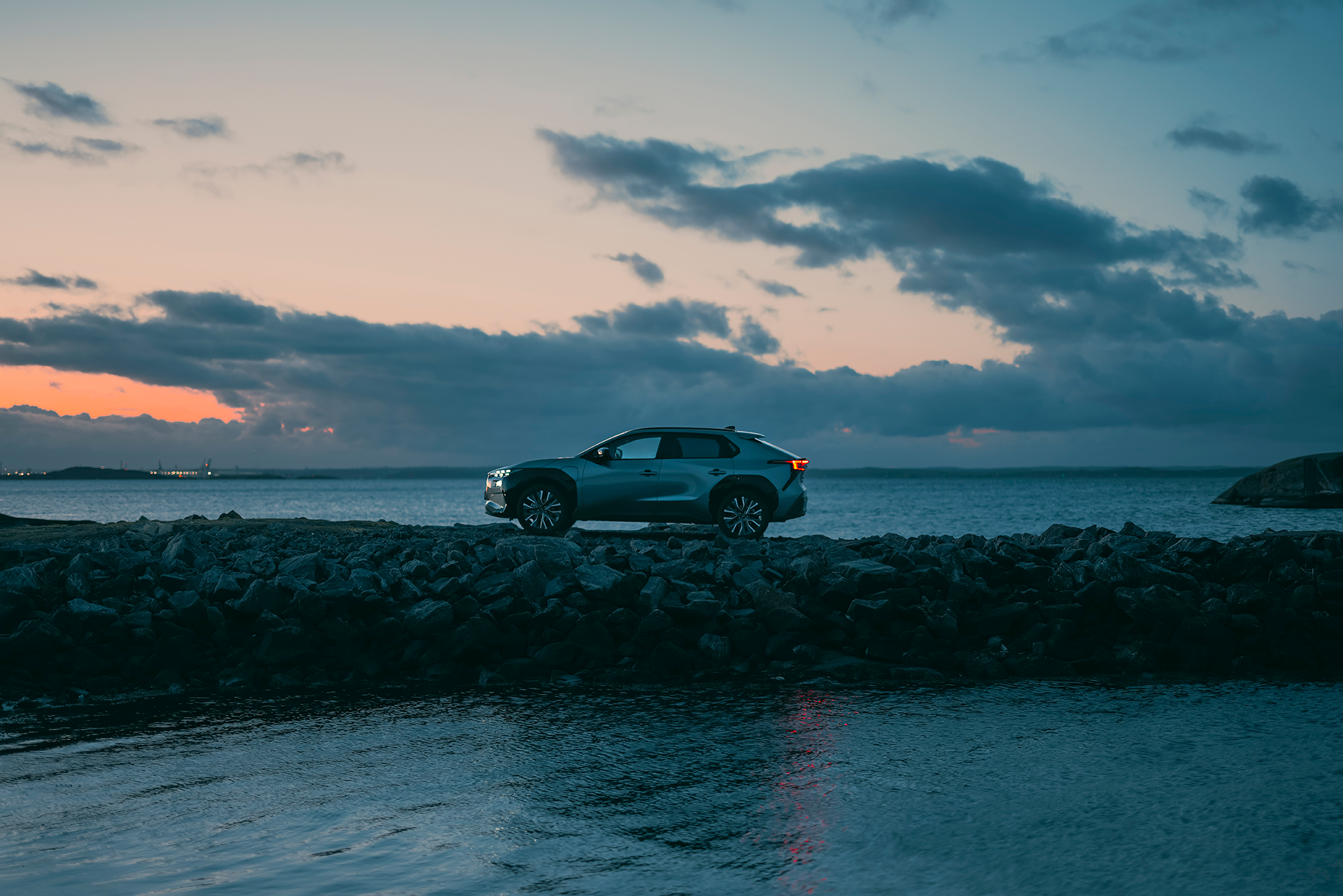 Subaru Solterra pysäköitynä kallioiselle merenrannalle auringonlaskun aikaan.