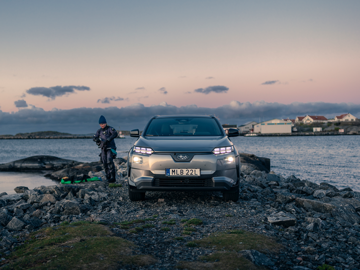 Subaru Solterra kallioisella rannikolla sukellusvarusteisiin pukeutuneen henkilön kanssa.
